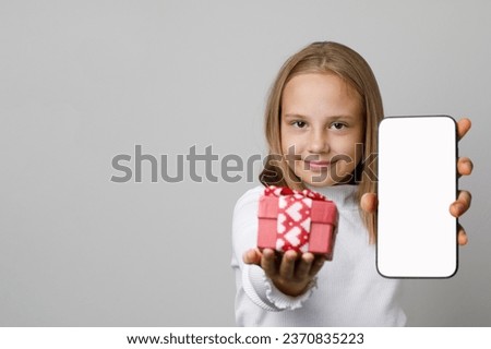 Christmas portrait of cheerful child in Santa hat holding gift and smartphone with blank empty white screen display