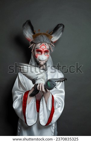 Fashion beauty portrait of perfect young woman rabbit with pigeon bird standing on black background. Halloween makeup and costume