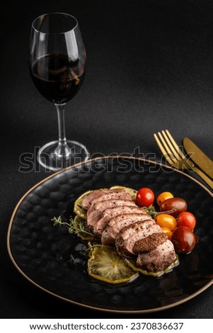 Roasted duck breast fillet on caramelized apples. the dish lies on a black plate on a black background. glass of red wine.