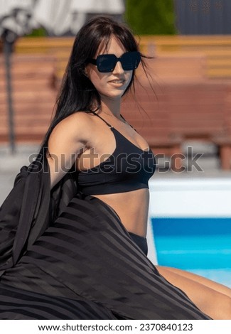 Portrait of a girl in a black swimsuit and glasses by the pool.