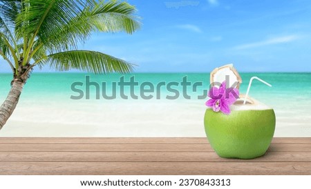 Coconut juice (coconut water) in fresh green coconut on wooden table with coconut palm tree on beach and blue sky blurred background. Vacation and holiday concept. Copy space.
