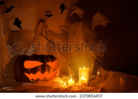 Spooky Jack o lantern carved pumpkin, spider web, ghost, bats and glowing light in dark. Happy Halloween! Scary atmospheric halloween party decorations, space for text. Trick or treat