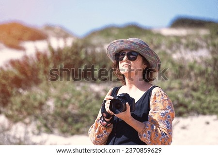 A female photographer with a hat photographing some dunes
