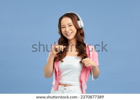 Image of young beautiful woman posing isolated over color background listening music with headphones.