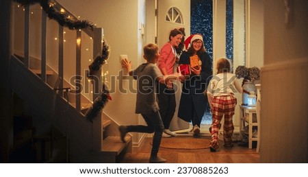 Grandmother Visiting Family for Christmas Holidays on a Snowy Winter Evening. Young Female Opening the House Door, Grandchildren Running to Meet Their Grandma with Holiday Gifts and Presents