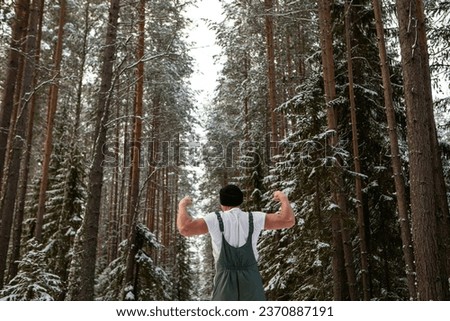 Young in a t-shirt man with athletic appearance in winter forest surrounded by snowflakes. Sport and cold acclimation concept. High quality photo