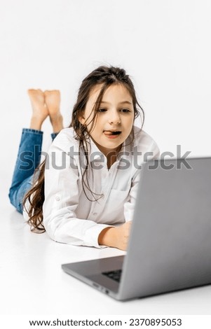The concept of childish, sincere emotions. A little girl watches a movie on a light background. The concept of advertising a happy childhood and bright emotions with modern technologies.
