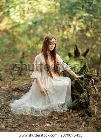 Portrait of  a beautiful red haired girl in light princesses dress and tiara near moss tree. Fairy tale story about elven.Amazing model posing in forest .Warm art work