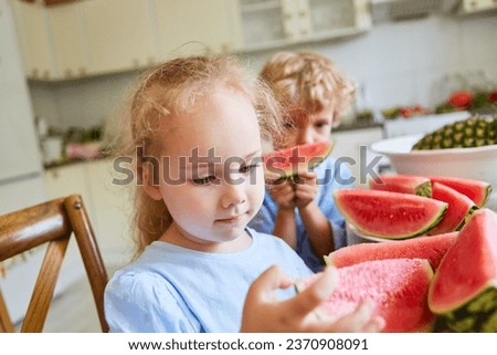Cute blond girl examining watermelon slices with brother in kitchen at home