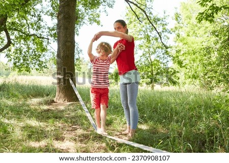 Mother supporting son doing slacklining in garden Royalty-Free Stock Photo #2370908107
