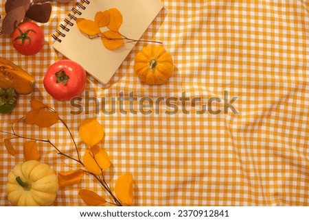 Creative checkered fabric background decorated with pumpkins, ripe tomatoes and autumn leaves. Autumn theme, creative decoration ideas for advertising. Space for product display, text and design