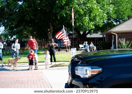 American lawn flags display front of modern pickup truck driving on residential street smalltown Fourth of July parade, Dallas, Texas, USA blurry crowd people waving hands. Independence Day patriot