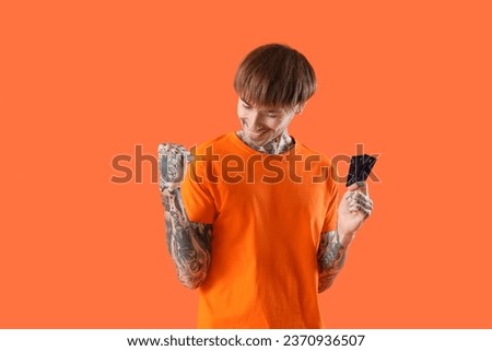 Happy young man with credit cards on orange background