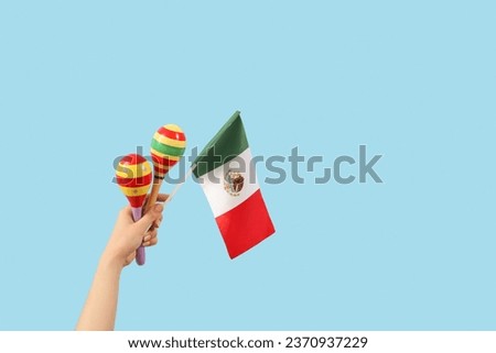 Female hand holding maracas and Mexican flag on blue background