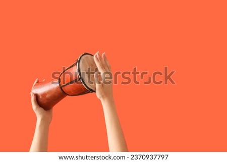 Female hands holding Mexican drum on orange background