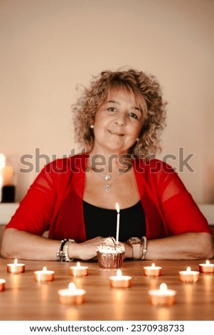 middle-aged woman in red t-shirt, looking at her birthday cupcake surrounded by candles