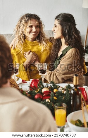 sweet lgbt couple holding hands and looking cheerfully at each other sitting at Christmas table