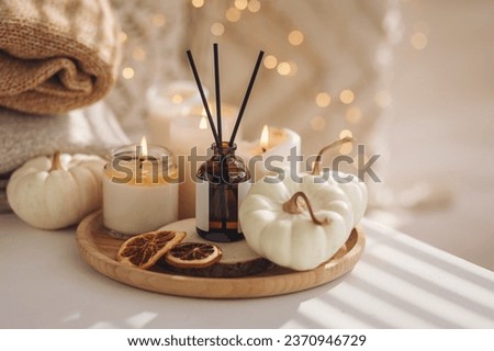 Home comfort, coziness, aromatherapy. Cozy fall interior with knitted wool warm sweater, burning candles and autumn aroma perfume diffuser in the bedroom. Pumpkin pie, cinnamon, anise