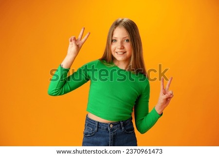 Teen girl makes peace or victory sign over yellow background