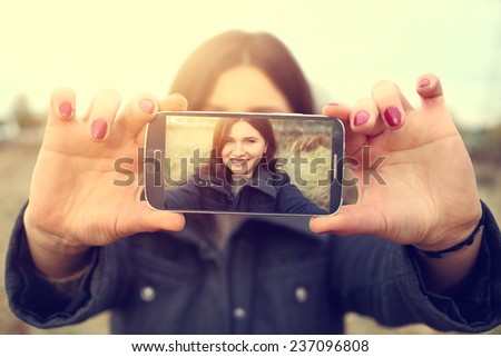 	Cute girl takes a picture of the phone on a sunny glade
