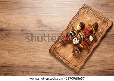 Delicious shish kebabs with vegetables on wooden table, top view. Space for text Royalty-Free Stock Photo #2370968657