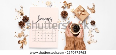Paper calendar for January with Christmas decorations and female hands with cup of coffee on light background