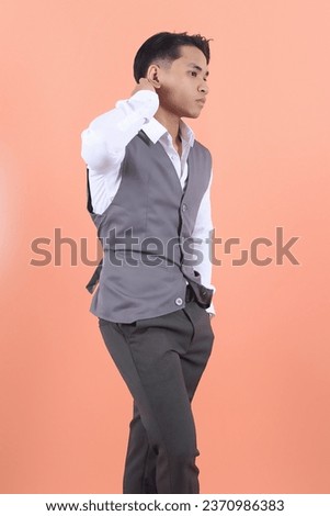 Handsome young Asian businessman wearing a suit vest is seen from the side holding his head back with one hand in a formal and confident manner, showing success
