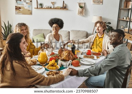 happy multiethnic family sitting at festive table praying and holding hands cheerfully, Thanksgiving