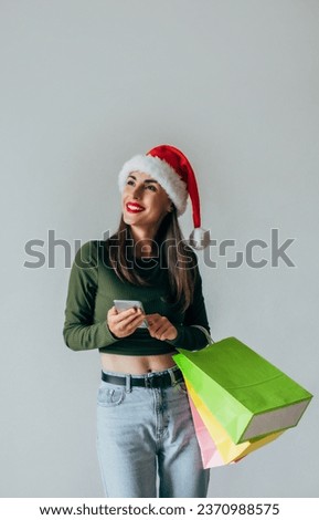 Close up photo of happy cute young girl while buying christmas gifts and typing modern smart phone on grey background. Happy New Year 2024 and Christmas time. Online shopping