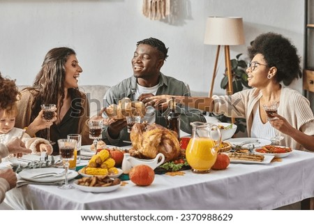 happy african american woman reaching baked buns near friends and family during Thanksgiving dinner