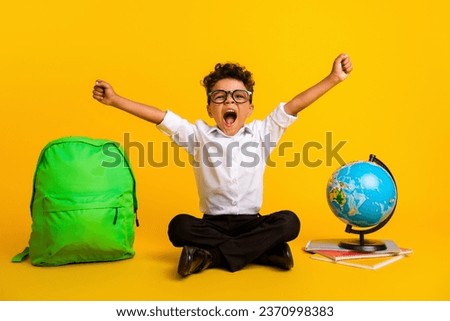Full size portrait of excited smart schoolchild sit floor raise fists world globe notebook bag isolated on yellow color background Royalty-Free Stock Photo #2370998383