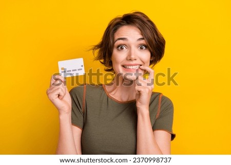 Photo of astonished impressed girl bob hairstyle dressed khaki t-shirt hold debit card biting finger isolated on yellow color background