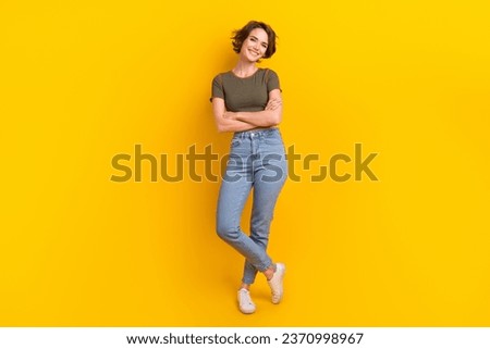 Full size photo of gorgeous adorable girl wear khaki t-shirt denim pants standing arms crossed isolated on yellow color background