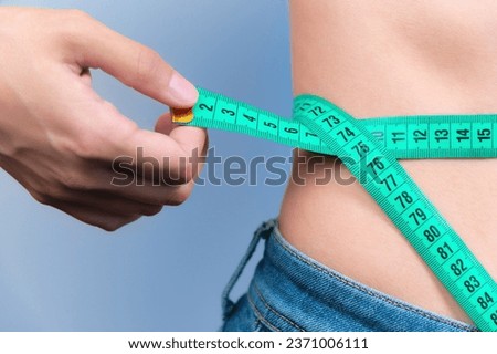 woman measures her waist with a tape measure. Diet and body weight control concept, close-up, toned. A girl in jeans takes measurements of her figure and weight loss Royalty-Free Stock Photo #2371006111