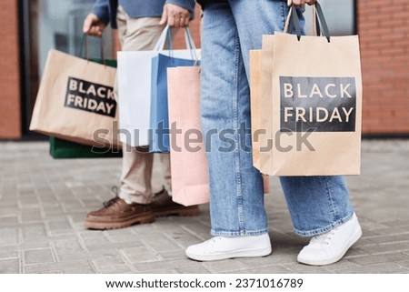 Side view of unrecognizable couple holding Black friday shopping bags walking together outdoors, copy space