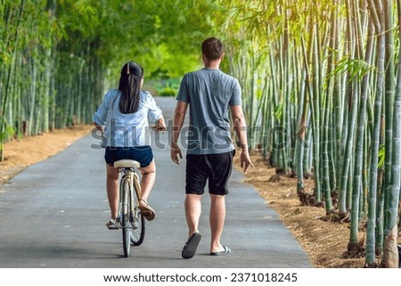 Happy Asian couple enjoy with bicycle in bamboo park. Asian lovers ride bicycle with having fun to exercise activity together in garden. Chilling and relaxing family enjoys nature. Selective focus.