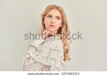 Feminine beauty. Portrait of a cute blonde girl with delicate pink makeup posing in an elegant white blouse on a pink studio background. Copy space. Hairstyles, Hollywood wave.