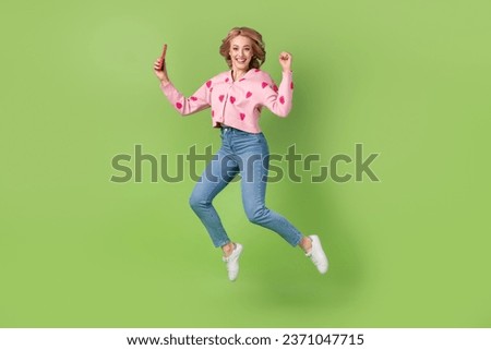 Full size photo of excited delighted girl jumping use smart phone blogging raise fist isolated on green color background