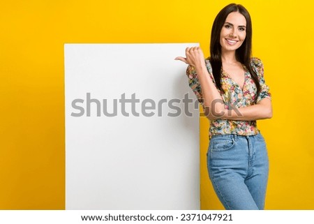 Portrait of optimistic woman with long hairstyle wear stylish dress directing at banner empty space isolated on yellow color background