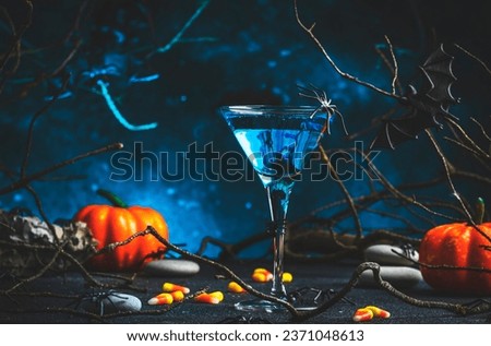 Halloween blue martini alcoholic cocktail on scary dark blue background with twisted branches, bats, stones and spiders,  festive drink for party