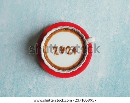Hello 2024 theme white coffee cups with number 2024 over frothy surface placed over red saucer flat lay on pastel blue background. Holidays food art Happy New Year. (top view)