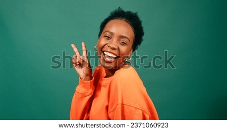 Happy young woman holds peace sign to eye, silly pose, green studio portrait