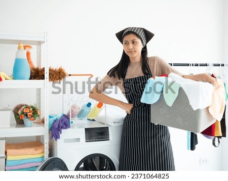 Asian young housewife tired cleaning clothes and towels alone without husband after use dryer machine and keep its in laundry basket in washing room at the house