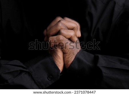 black man praying to god with hands together on black background with people stock image stock photo