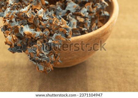 Dry petals of blue hydrangea inflorescence in a wooden bowl standing on the table. Brown tablecloth. Home decor, dried flowers, natural colors concept  Nobody. Copy space.
