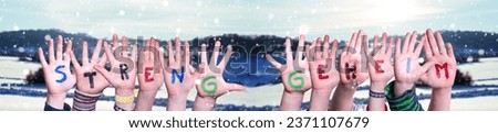 Children Hands Building Colorful German Word Streng Geheim Means Top Secret. White Winter Background With Snowflakes And Snowy Landscape.