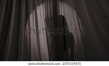 Medium shot of a young woman's silhouette wrapped in a towel standing behind the curtain, flirting on a semi-transparent glowing background in a muffled light. Royalty-Free Stock Photo #2371119571