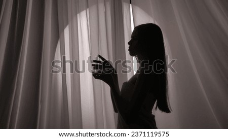 Medium side view shot of a young woman silhouette wrapped in a towel holding a jar of body, face cream, beauty product in a muffled light. Royalty-Free Stock Photo #2371119575