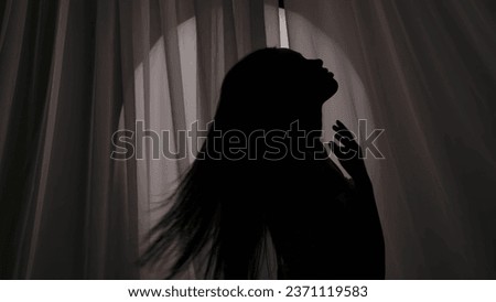 Medium shot of a young woman's silhouette wrapped in a towel touching, caressing her body, neck and swishing her hair in a muffled light. Royalty-Free Stock Photo #2371119583