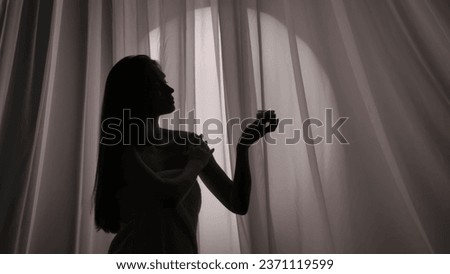 Medium side view shot of a young woman's silhouette wrapped in a towel holding a jar of body, face cream and applying the substance on her skin in a muffled light. Royalty-Free Stock Photo #2371119599